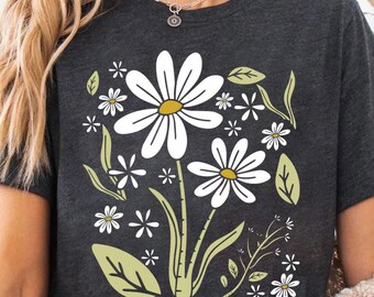 May include: Dark gray t-shirt featuring a floral design with white daisies and green leaves. The graphic tee has a crew neck and short sleeves. The floral design includes several sizes of daisies and other small flowers.