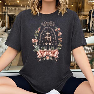 May include: A charcoal gray short-sleeve t-shirt featuring a central graphic of a cross, the letter M, and two hearts surrounded by a floral wreath. The text reads, O Mary, Conceived Without Sin, Pray for Us Who Have Recourse to Thee.