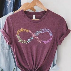 May include: A maroon t-shirt with a rainbow floral infinity symbol design. The shirt is made of a soft, comfortable material and has a relaxed fit.