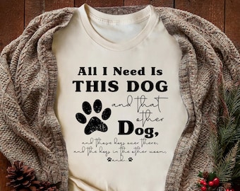 May include: A white t-shirt with a black paw print and the text "All I Need Is THIS DOG and that other Dog, and these dogs over there, and the dogs in the other room, and..." printed on it.