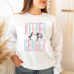 May include: White sweatshirt with the text "KEEPER of the GENDER" in pink, blue, and black lettering.