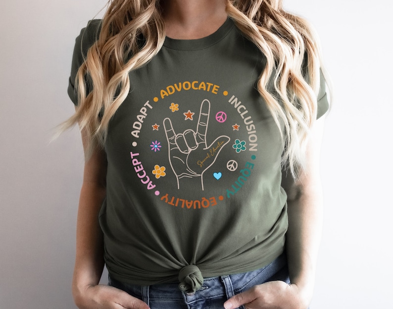 May include: A green t-shirt with a circle graphic featuring the American Sign Language symbol for "I love you" surrounded by the words "Accept", "Adapt", "Equality", "Equity", "Advocate", "Inclusion".