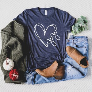 May include: A navy blue t-shirt with a white heart design and the word "gigi" inside the heart.