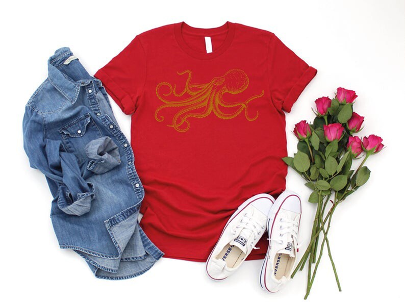 May include: A red t-shirt with a gold octopus design, paired with a denim shirt, white sneakers, and a bouquet of pink roses. The casual ensemble suggests a relaxed, everyday style.