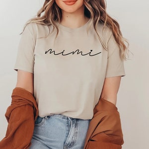 May include: A beige t-shirt with the word "mimi" written in black cursive script.
