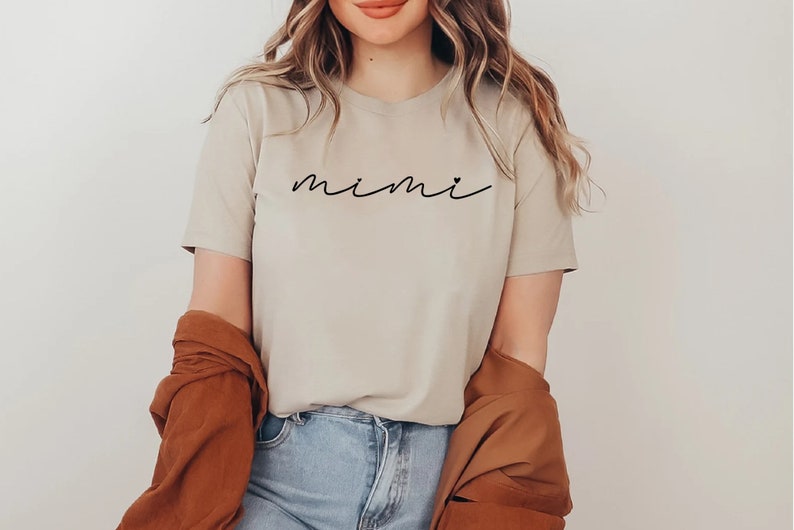 May include: A beige t-shirt with the word "mimi" written in black cursive script.