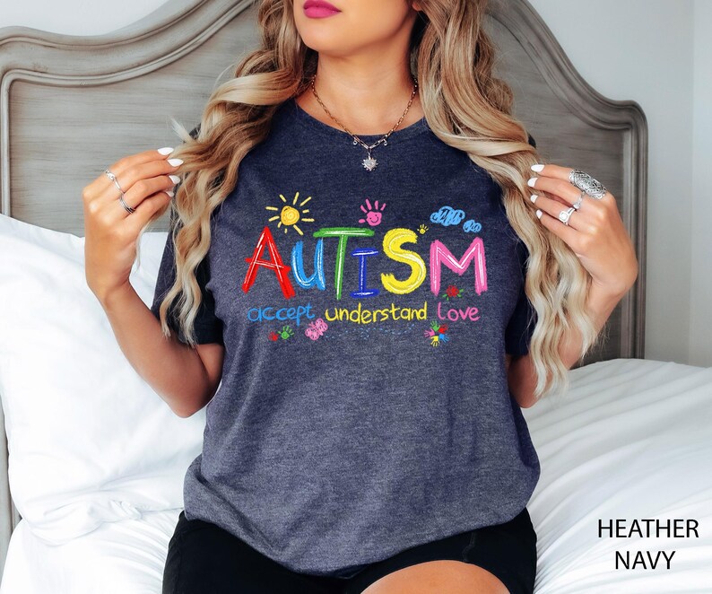 May include: Heather navy t-shirt with the word "AUTISM" in colorful embroidered letters, along with the phrases "accept understand love" and small graphics of a sun, handprints, clouds, and flowers.