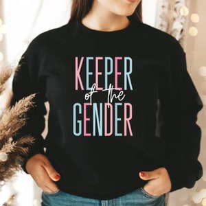 May include: A black sweatshirt with the text "KEEPER of the GENDER" in pink and blue lettering.