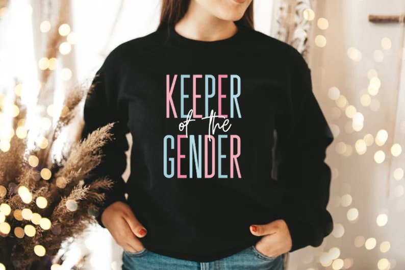 May include: A black sweatshirt with the text "KEEPER of the GENDER" in pink and blue lettering.