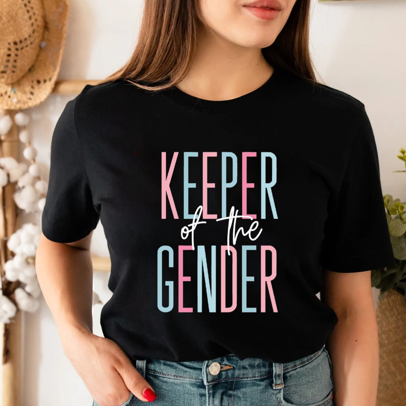 May include: A black t-shirt with the text "KEEPER of the GENDER" in pink and blue lettering.
