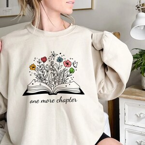 May include: A beige sweatshirt with a graphic of an open book with flowers growing out of it. The text "one more chapter" is printed below the book.