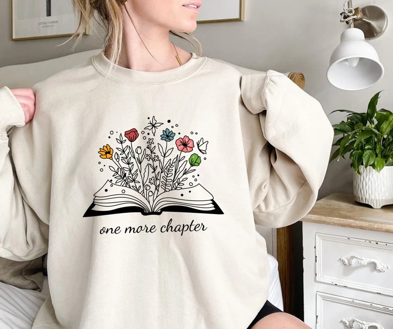 May include: A beige sweatshirt with a graphic of an open book with flowers growing out of it. The text "one more chapter" is printed below the book.