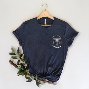 May include: A dark blue t-shirt with a white graphic of a medical symbol and the text "Emergency Department" in a circle.