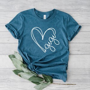 May include: A teal blue t-shirt with a white heart design and the word "Gigi" written inside the heart.