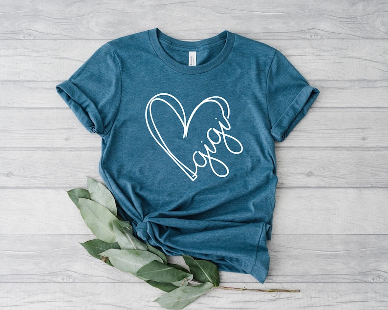 May include: A teal blue t-shirt with a white heart design and the word "Gigi" written inside the heart.