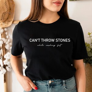 Puede incluir: Camiseta negra con texto blanco que dice "CAN'T THROW STONES while washing feet"