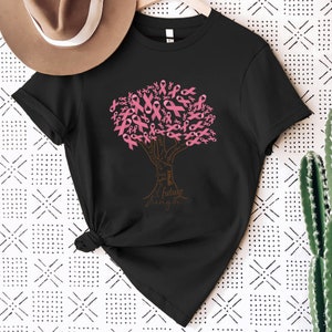 May include: A black short-sleeved t-shirt featuring a graphic of a tree where the leaves are composed of pink awareness ribbons. The trunk and branches contain the words cure, hope, faith, grace, fighter, together, future, and strength.
