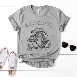 May include: A gray t-shirt with a black and white illustration of mushrooms and a crescent moon design. The shirt has a crew neck and short sleeves.