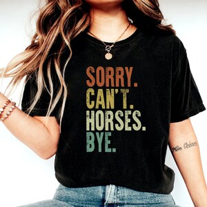 May include: A black cropped t-shirt with a vintage-style graphic that reads "SORRY. CAN'T. HORSES. BYE."