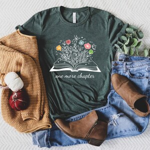 May include: A dark green t-shirt with a white graphic of an open book with flowers growing out of it. The text "one more chapter" is printed below the book.