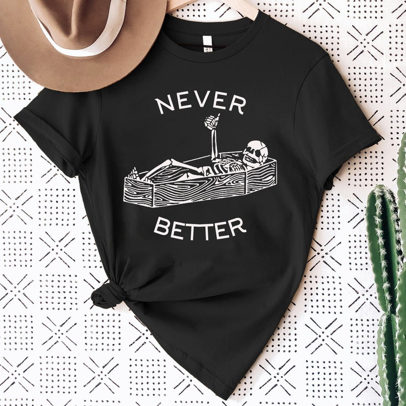 May include: Black t-shirt with a white graphic of a skeleton in a coffin with the text "NEVER BETTER" above the coffin.