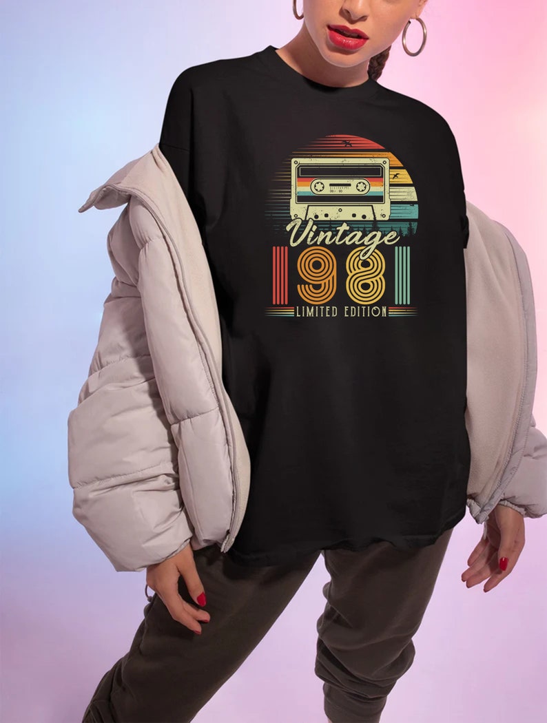 May include: Black t-shirt featuring a retro design with a cassette tape, a sunset, and the text "Vintage 1981 Limited Edition" in a vintage font. The design incorporates shades of orange, yellow, green, and blue.