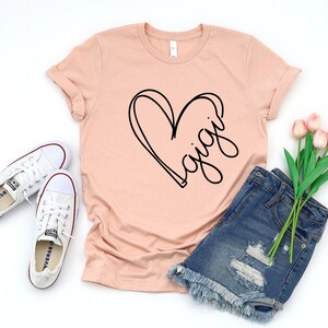 May include: A peach-colored t-shirt with a black heart and the word "Gigi" written inside the heart.