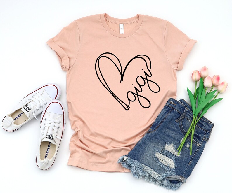 May include: A peach-colored t-shirt with a black heart and the word "Gigi" written inside the heart.