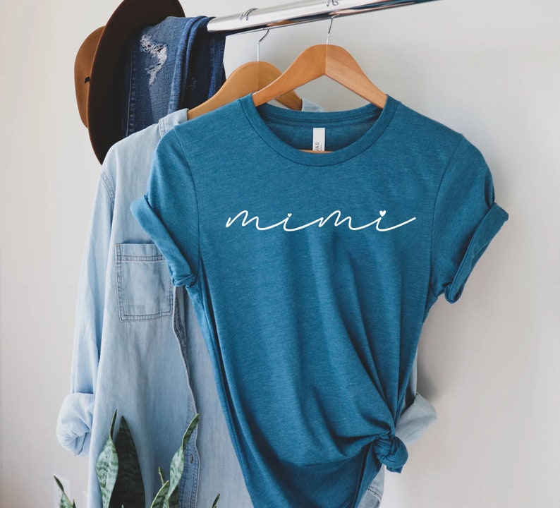 May include: A teal blue t-shirt with the word "mimi" written in white cursive with a small white heart after the "i".