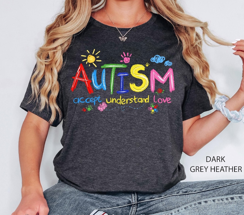 May include: Dark grey heather t-shirt with the word "AUTISM" in colorful embroidered letters. The shirt also features the words "accept understand love" and colorful graphics of a sun, clouds, and flowers.