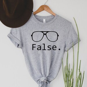 May include: Grey t-shirt with a black graphic of sunglasses and the word "False."