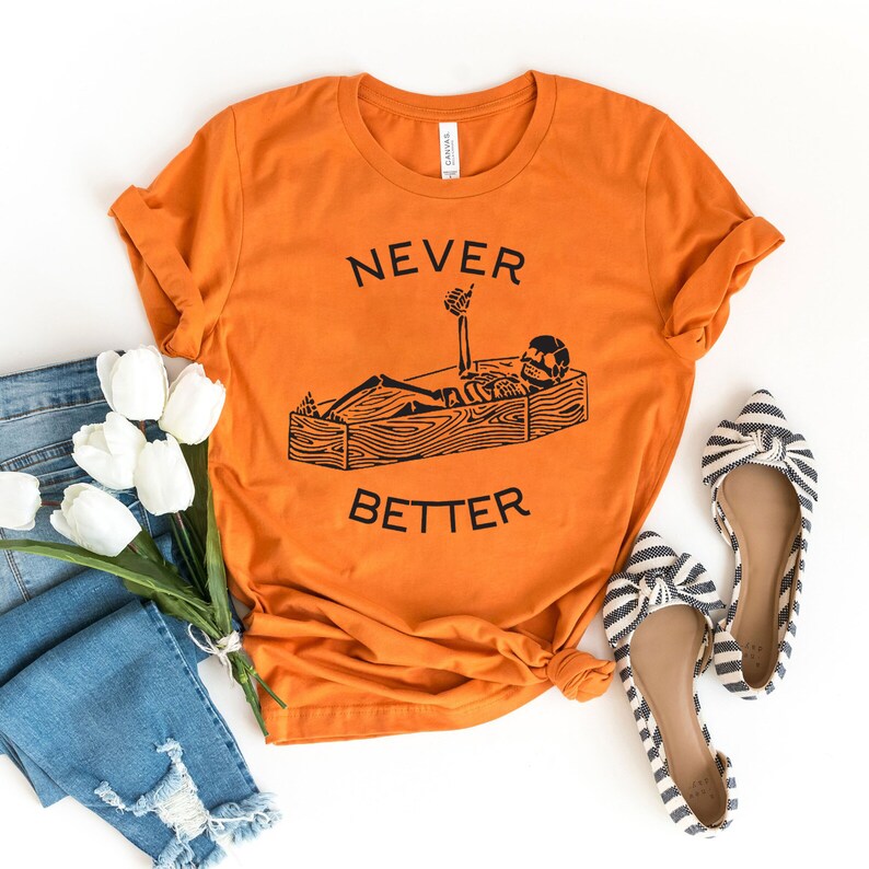 May include: Orange t-shirt with a black skeleton graphic lying in a coffin and the text "NEVER BETTER".