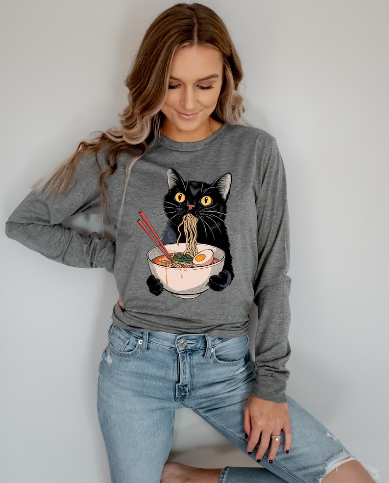 May include: A gray long-sleeved shirt with a black cat eating ramen noodles from a bowl. The cat has yellow eyes and is wearing a red headband.