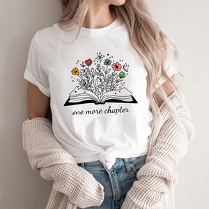 May include: White t-shirt with a black and white illustration of an open book with colorful flowers growing out of it. The text "one more chapter" is printed below the book.