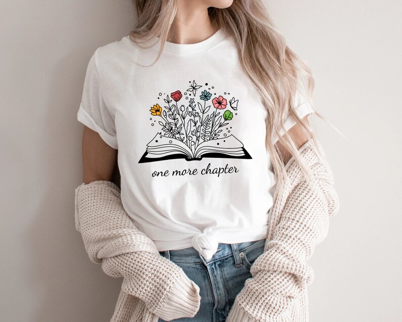 May include: White t-shirt with a black and white illustration of an open book with colorful flowers growing out of it. The text "one more chapter" is printed below the book.