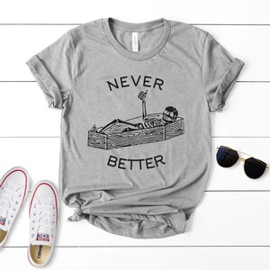 May include: Gray t-shirt with a black skeleton in a coffin giving a thumbs up. The text "NEVER BETTER" is printed on the shirt.