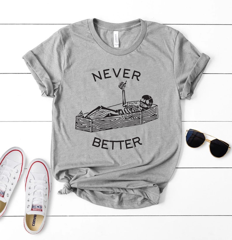 May include: Gray t-shirt with a black skeleton in a coffin giving a thumbs up. The text "NEVER BETTER" is printed on the shirt.