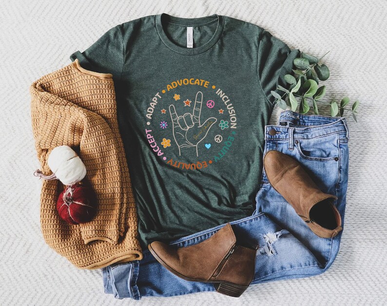 May include: A dark green t-shirt with a circle graphic featuring the words "Adapt, Accept, Advocate, Ally, Equity, Inclusion" and a hand making the American Sign Language sign for "I love you".