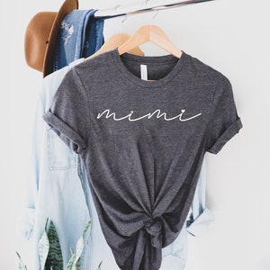 May include: A dark gray t-shirt with the word "mimi" written in white cursive script with two small hearts on either side of the word.