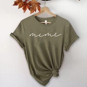 May include: A green t-shirt with the word "mimi" written in white cursive with a small heart above the "i".