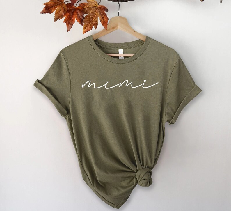 May include: A green t-shirt with the word "mimi" written in white cursive with a small heart above the "i".