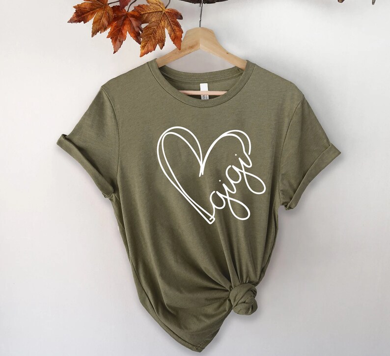 May include: A green short-sleeved t-shirt with a white heart design and the word "Gigi" written inside the heart.