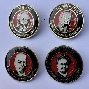 May include: Four round pins with gold trim, each featuring a black and white portrait of a historical figure. The pins have red backgrounds and black borders with white text. The text on the pins reads "Karl Marx 1818-1883", "Friedrich Engels 1820-1895", "V.I. Lenin 1870-1924", and "Leon Trotsky 1879-1940". All pins have the text "Revolutionary Communist International" around the border.