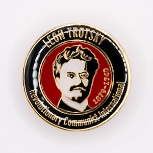 May include: A gold-colored pin with a black and red circular design. The center features a black and white portrait of Leon Trotsky with the text "Leon Trotsky 1879-1940 Revolutionary Communist International".