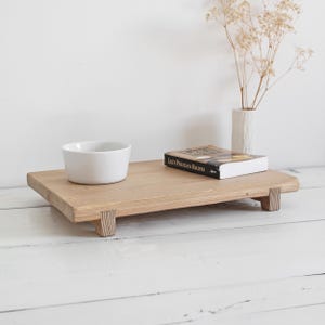 Könnte beinhalten: Ein Holztablett mit vier Beinen, einer weißen Schüssel und einem Buch mit dem Titel "Lily's Priceless Recipes" darauf. Das Tablett ist aus hellem Holz gefertigt und hat eine natürliche Oberfläche.