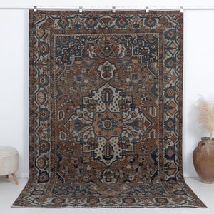 May include: A large rectangular area rug featuring a complex geometric and floral pattern in shades of brown, navy blue, and cream. The design includes a central medallion surrounded by intricate borders and symmetrical motifs throughout the field.