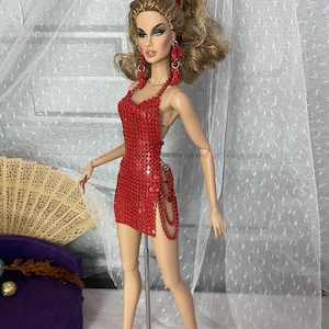 May include: A red sequined mini dress with a halter neckline and a side slit. The dress is on a doll stand and the doll is wearing red heels.
