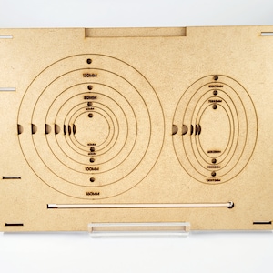 Könnte beinhalten: Ein Holzbrett mit zwei Sätzen konzentrischer Kreise, ein Satz mit Maßen in Millimetern von 40 mm bis 130 mm und der andere Satz mit Maßen in Millimetern von 120 mm bis 180 mm. Das Brett wird zum Erstellen von Kreisformen verwendet.