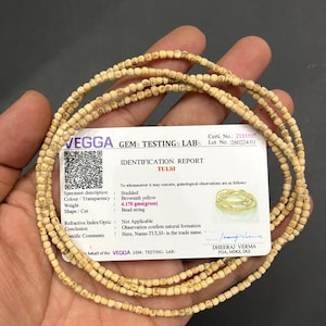 May include: A necklace made of small, light-colored, square beads. The necklace is displayed with an identification report card that reads "TULSI" and lists gemological observations. The beads weigh 4.170 grams.