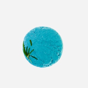May include: A round, light blue solid shampoo bar with a textured surface. A sprig of green rosemary is placed on the top of the bar. The bar is set against a white background.